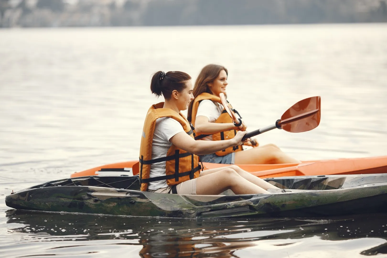 Two Girls wearing life jackets, paddling the kayaks in the water.