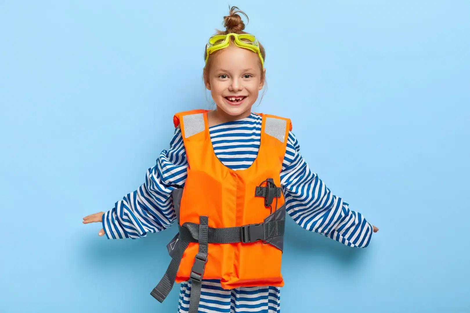 A cheerful girl wearing protective goggles, orange lifejacket, ready for a swimming session.