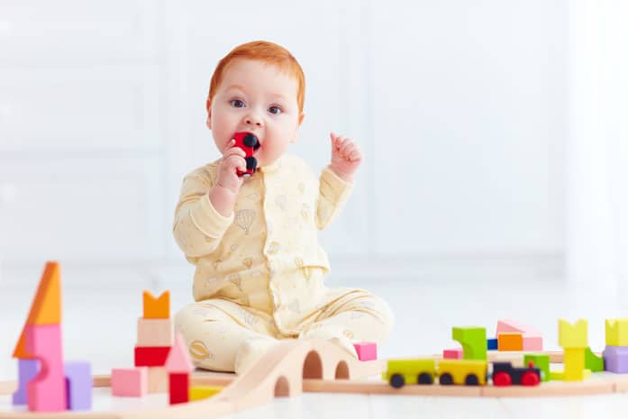 Cute ginger baby playing with toy railway road at home.
