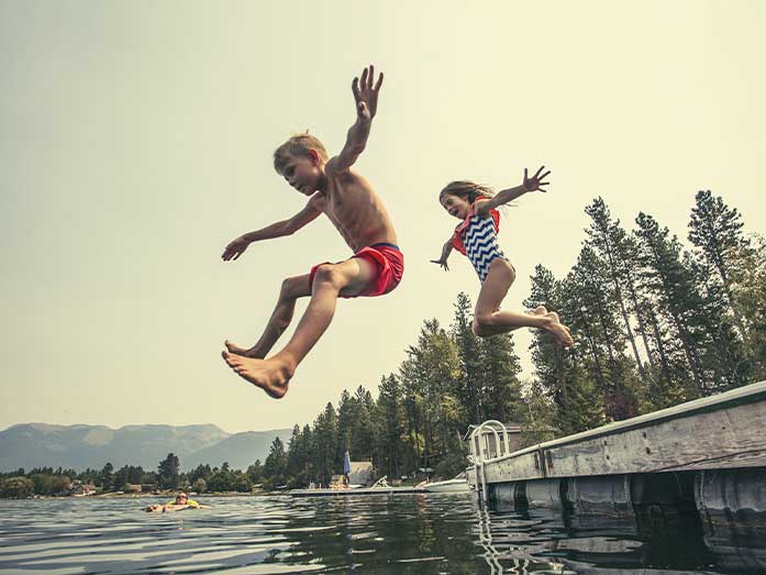 Kids jumping off the dock into a beautiful mountain lake. Having fun on a summer vacation at the lake with friends