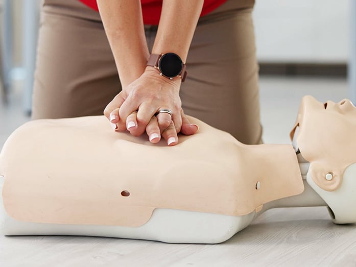 A student performing chest compressions on a CPR training mannequin during a first aid course.