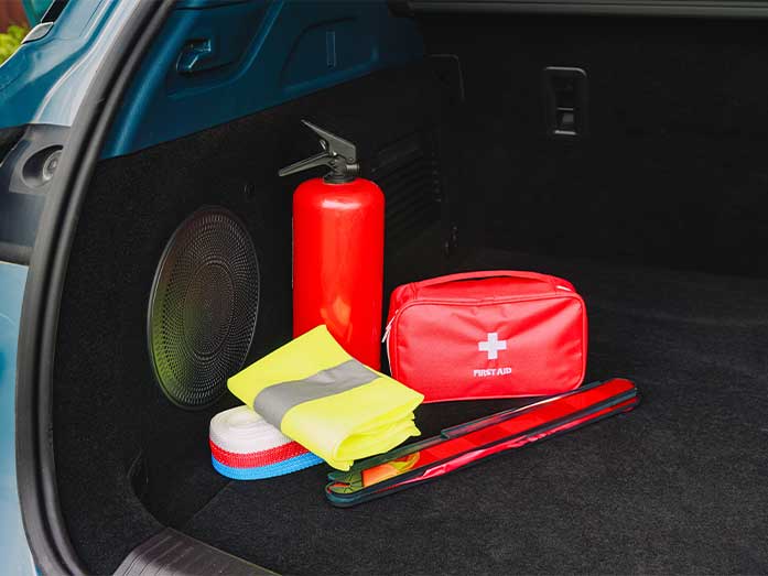Car trunk stocked with emergency preparedness supplies including a fire extinguisher, first aid kit, reflective safety vest, and warning triangle for roadside safety.